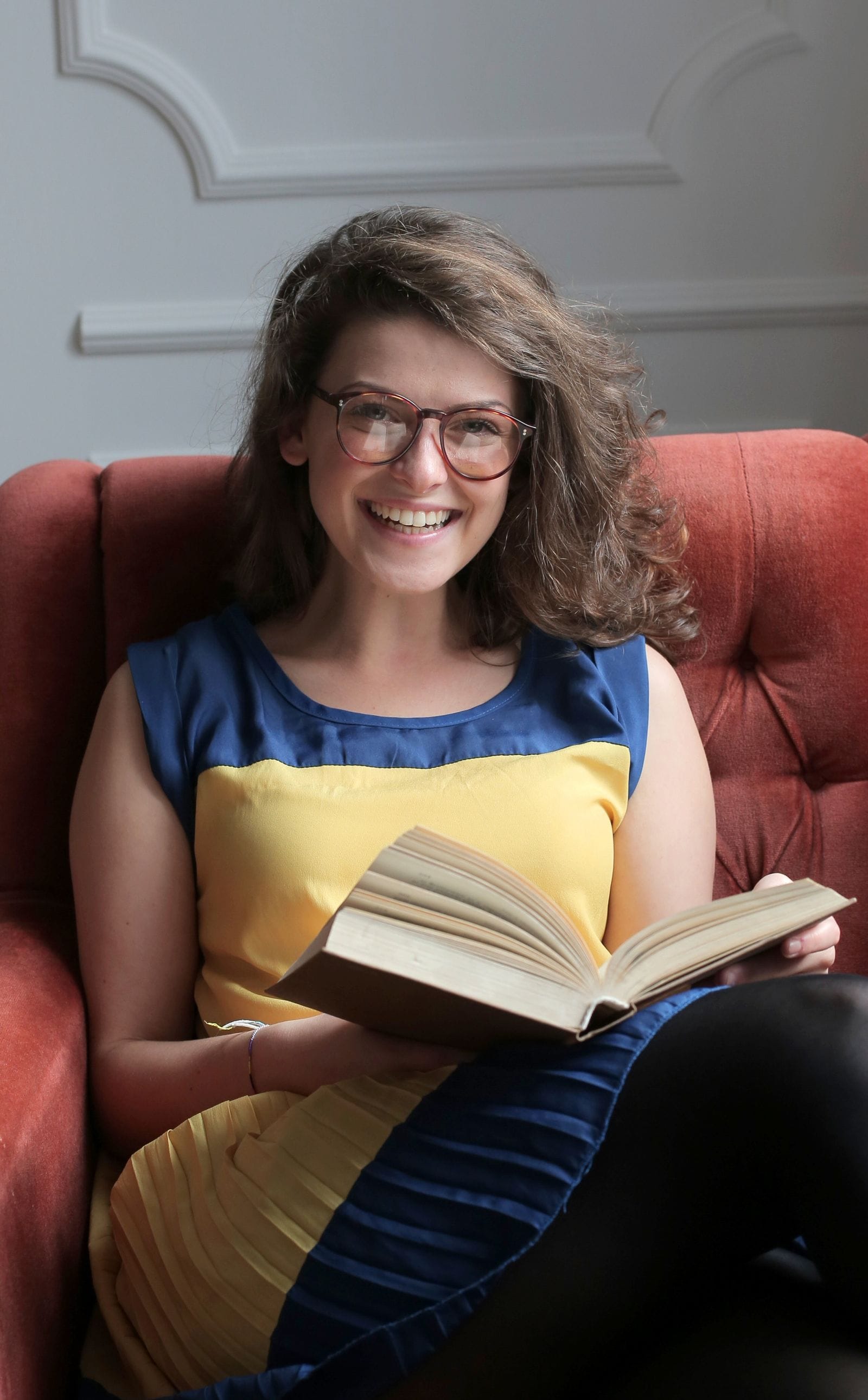 Mujer con lentes sonriendo con un libro abierto